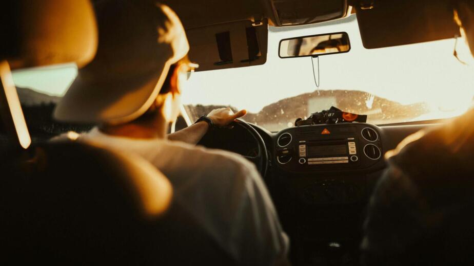 Man driving car with passenger at sunset, capturing warm sunlit atmosphere.