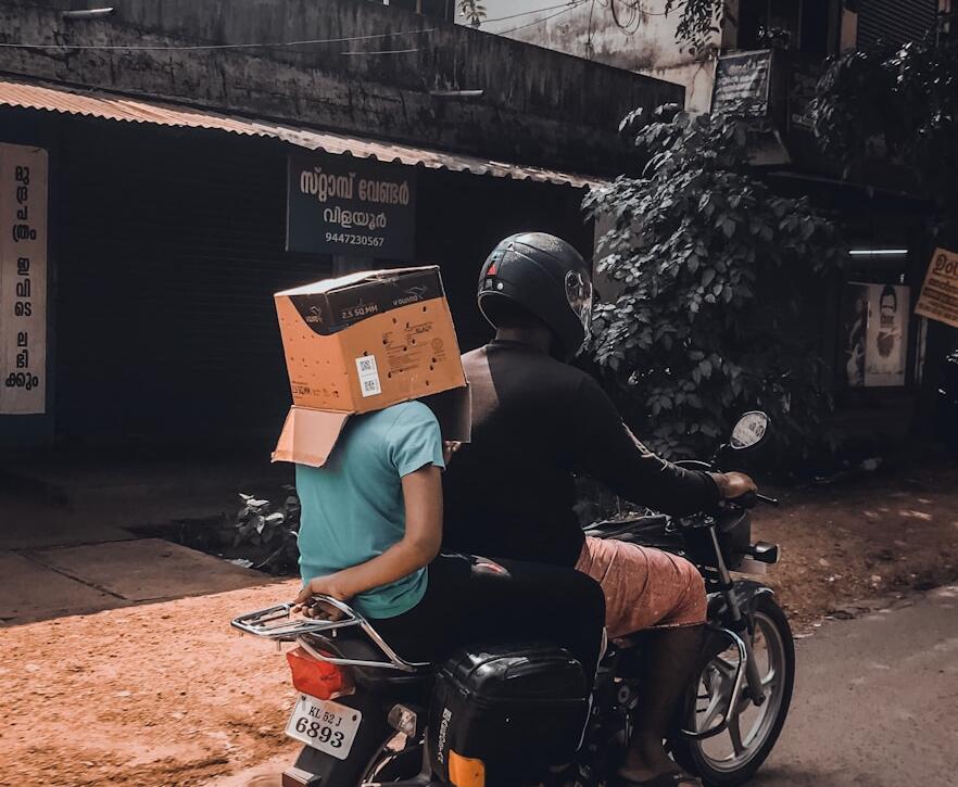 man riding motorcycle with person on his back with box on head
