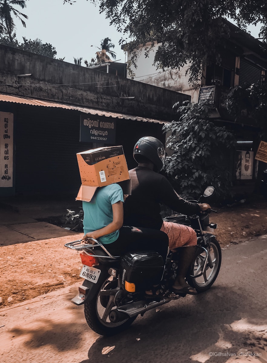 man riding motorcycle with person on his back with box on head