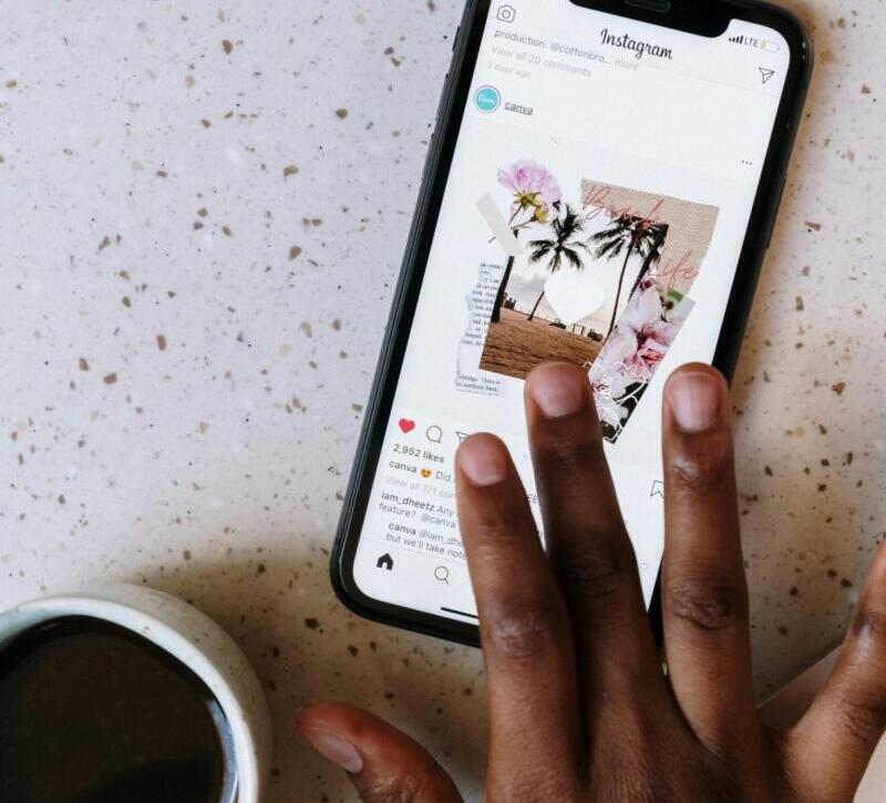 Close-up of hand scrolling Instagram on smartphone near coffee cup on table.