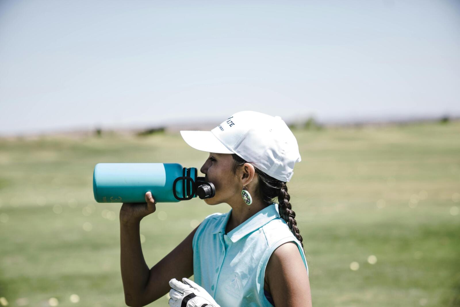 Woman golfer taking a break to hydrate on a sunny day in a field.