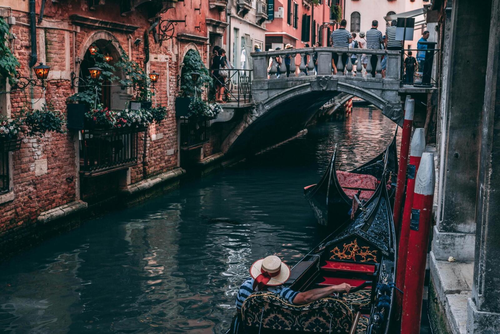A scenic view of a gondola passing under a traditional Venetian bridge in vibrant Venice.