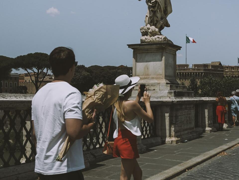 man in white t-shirt and black shorts standing on gray concrete pathway