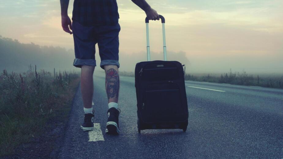 Man walking with a suitcase along a foggy road at sunrise, symbolizing adventure and travel.