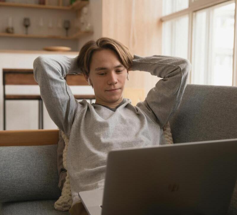 Young man comfortably working on a laptop in a cozy home setting, enjoying remote work lifestyle.