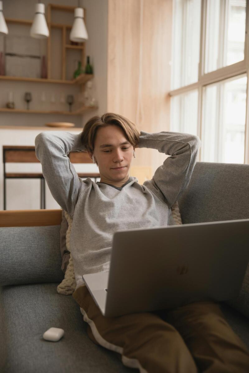 Young man comfortably working on a laptop in a cozy home setting, enjoying remote work lifestyle.