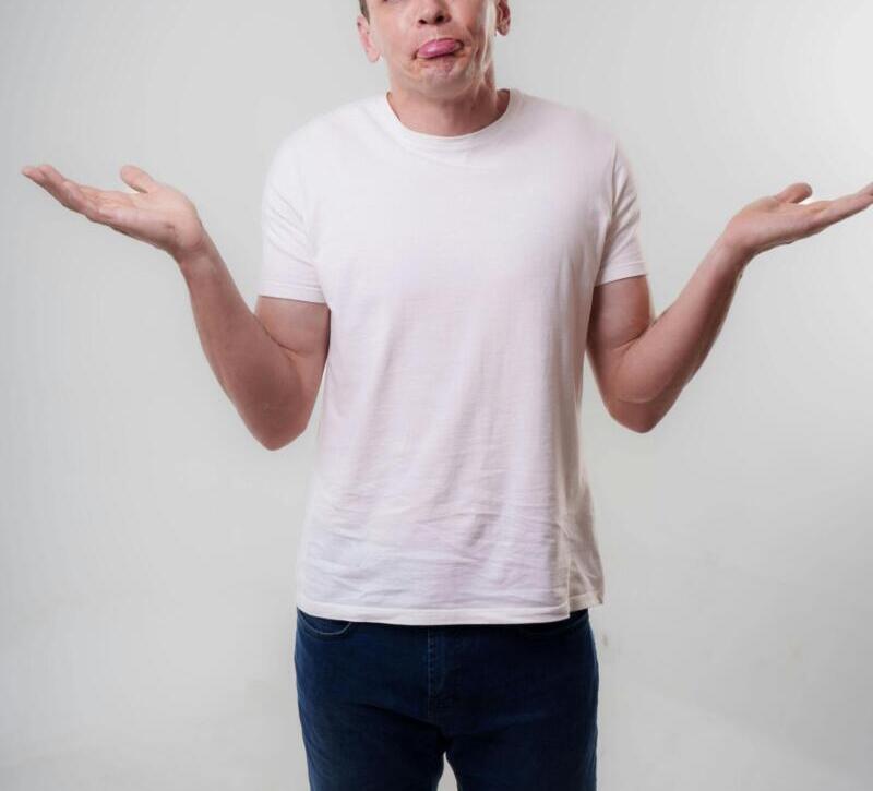 A young adult man in casual clothing shrugs with a neutral expression in a studio setting.
