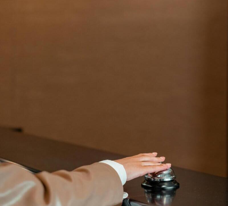 Elegant hand pressing a reception bell on a hotel counter, inviting service.