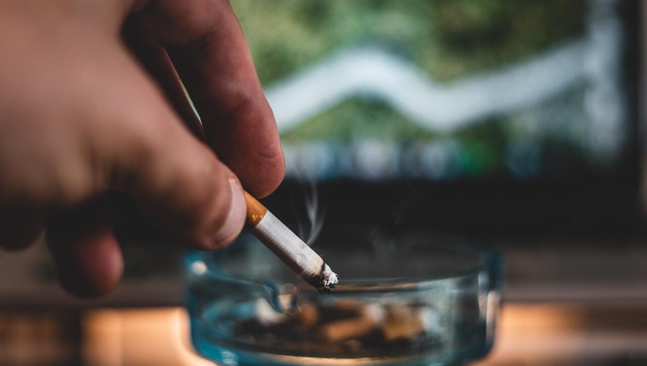 person holding cigarette stick and round glass ashtray