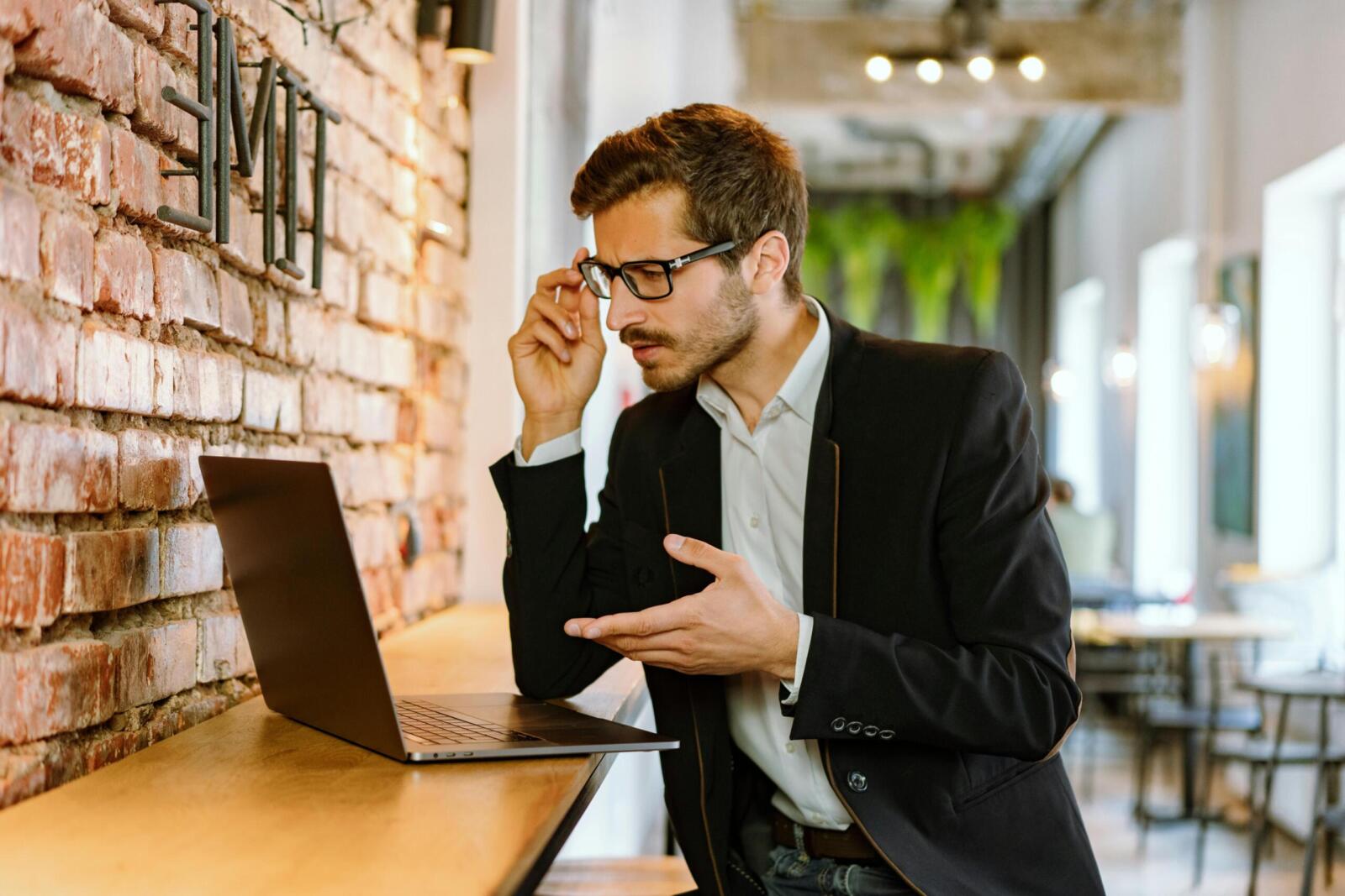 Businessman in a stylish black jacket using a laptop indoors, focused on his work.