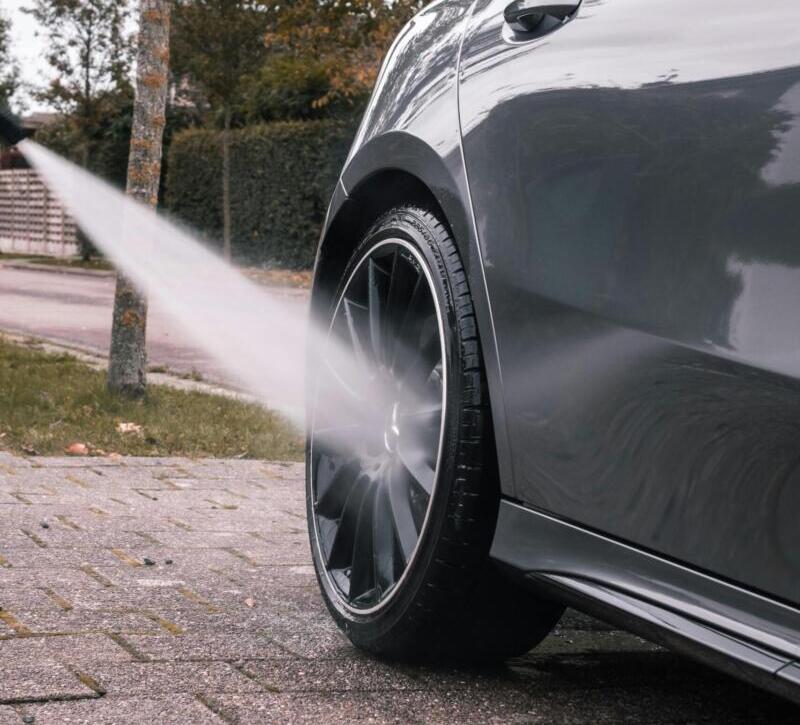 Close-up of a car wheel being cleaned with a high-pressure water stream on a sidewalk.