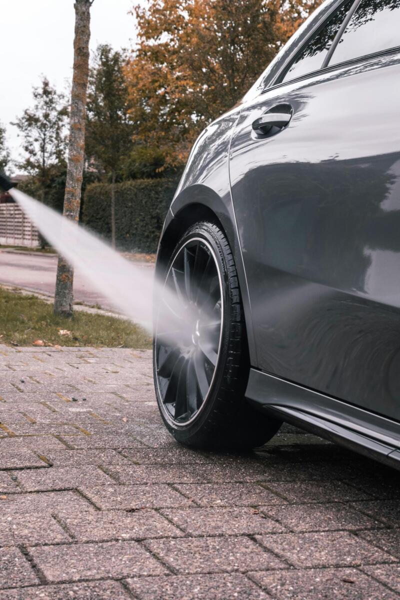 Close-up of a car wheel being cleaned with a high-pressure water stream on a sidewalk.