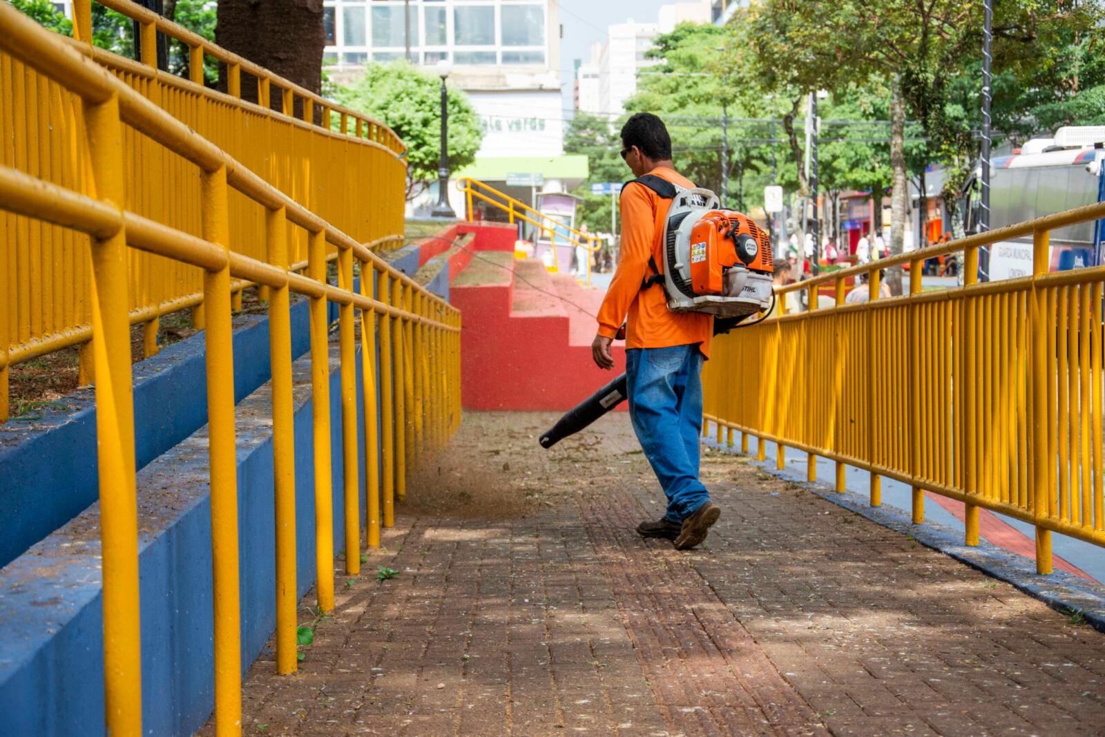 A worker uses a leaf blower to clean a colorful urban sidewalk in Londrina, Brazil.
