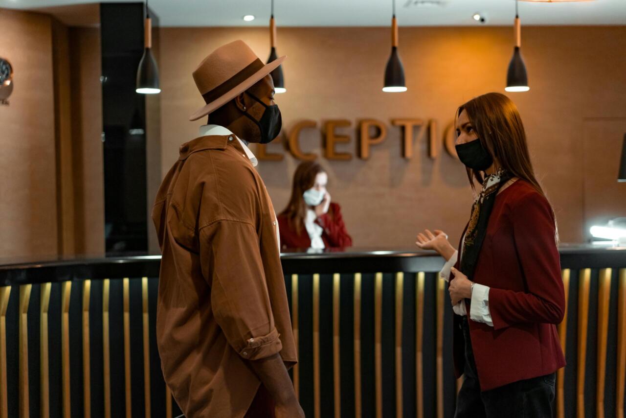 Two people in face masks interacting at a hotel reception desk during the COVID-19 pandemic.