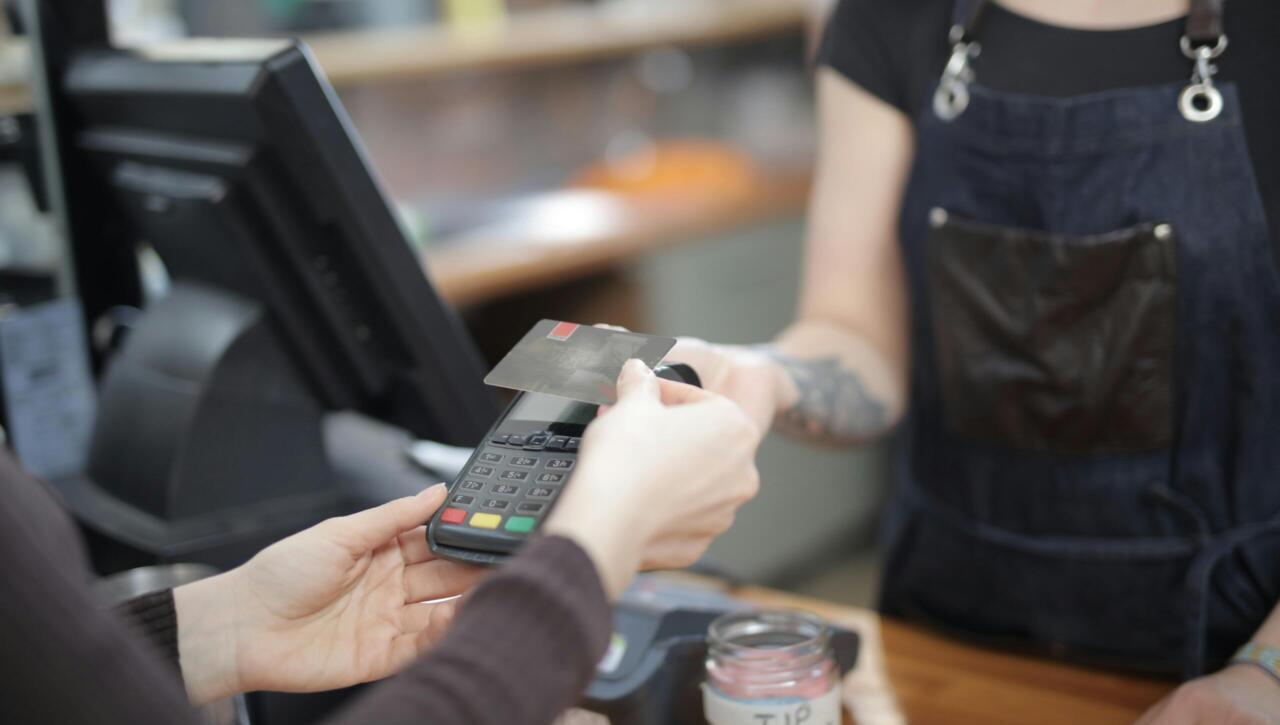 Close-up of customer and cashier during a credit card transaction at a store counter indoors.