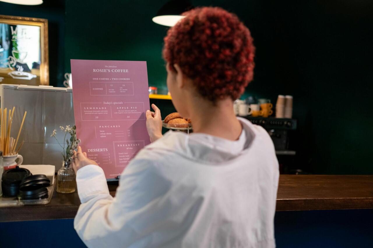 A woman with afro hair in a cafe, reading a menu with daily specials on offer.