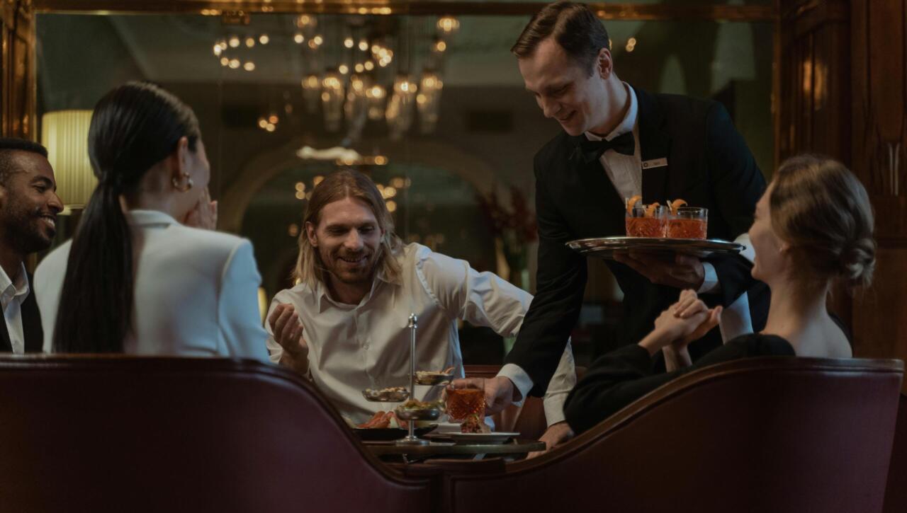 Group enjoying a classy dinner with a waiter serving appetizers in a luxurious setting.