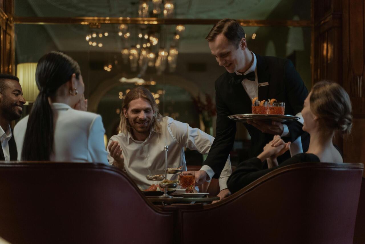 Group enjoying a classy dinner with a waiter serving appetizers in a luxurious setting.