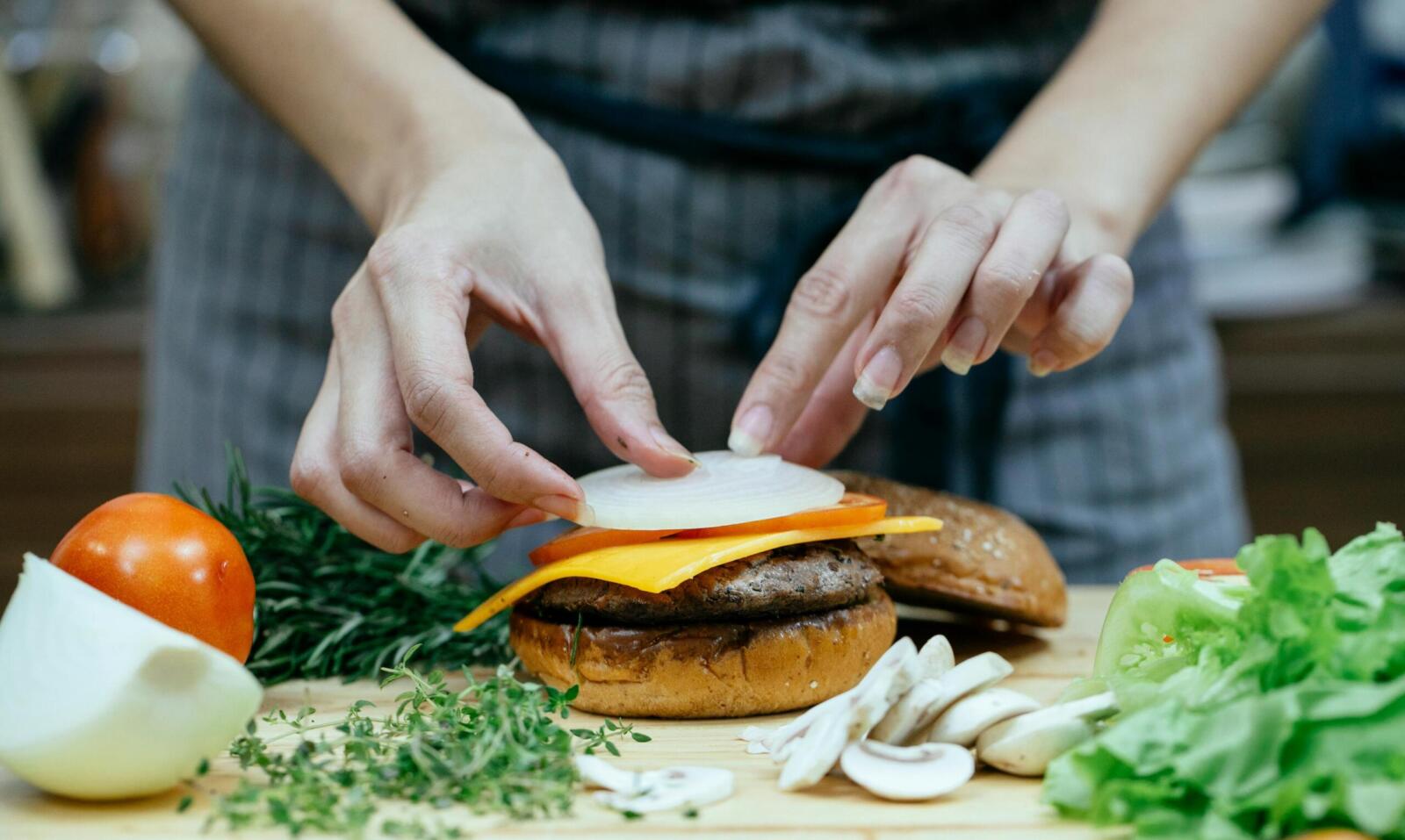 Close-up of a woman preparing a gourmet burger with fresh ingredients in a modern kitchen.