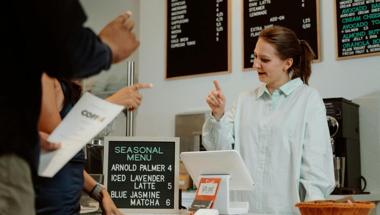Barista serving customers at cafe counter with seasonal menu board.