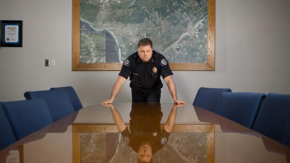 man in black t-shirt standing beside brown wooden table