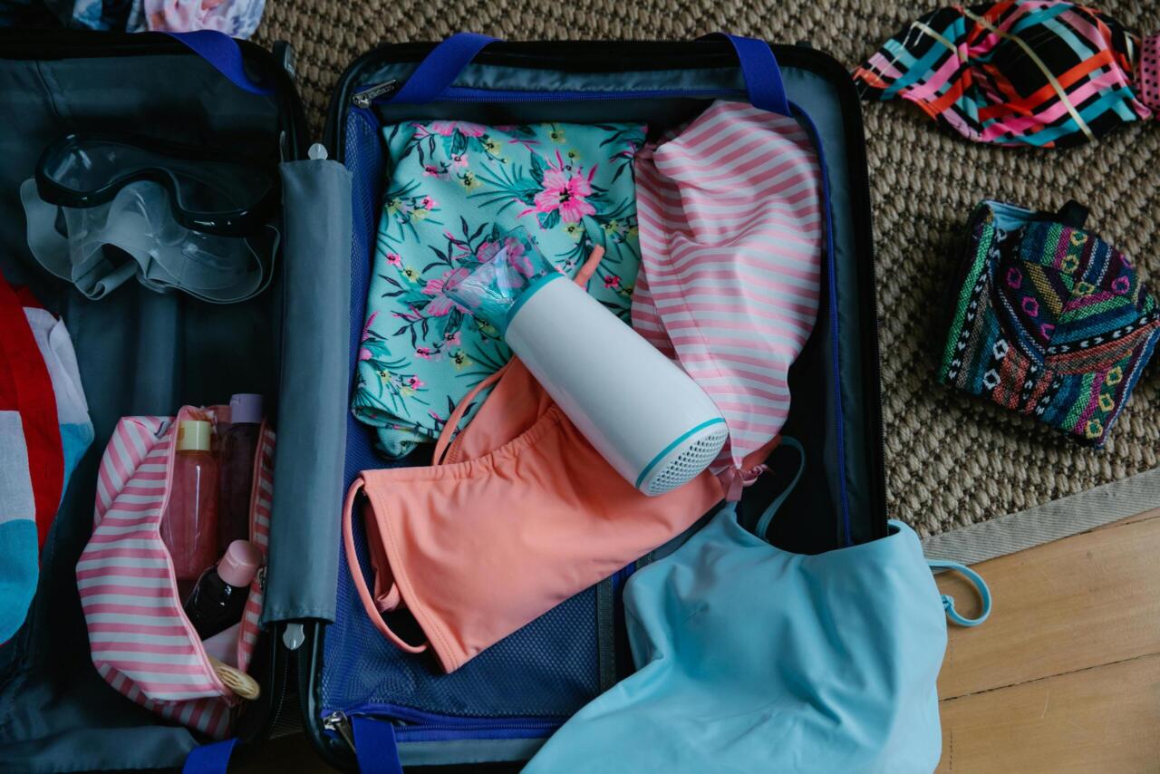 A packed suitcase with swimwear, goggles, and essentials for a summer trip.