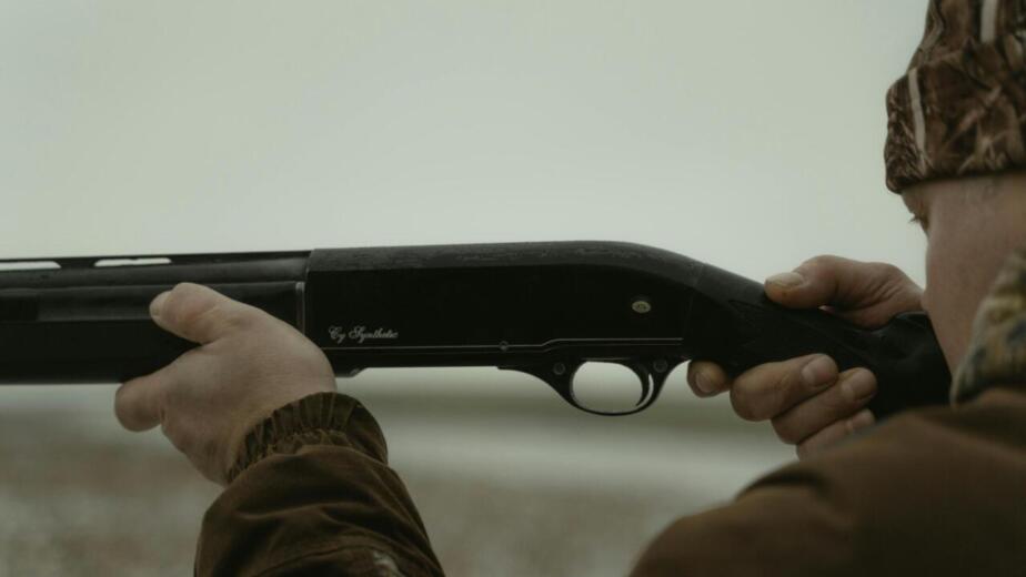 Close-up of a man holding a shotgun ready to aim outdoors, ideal for hunting themes.