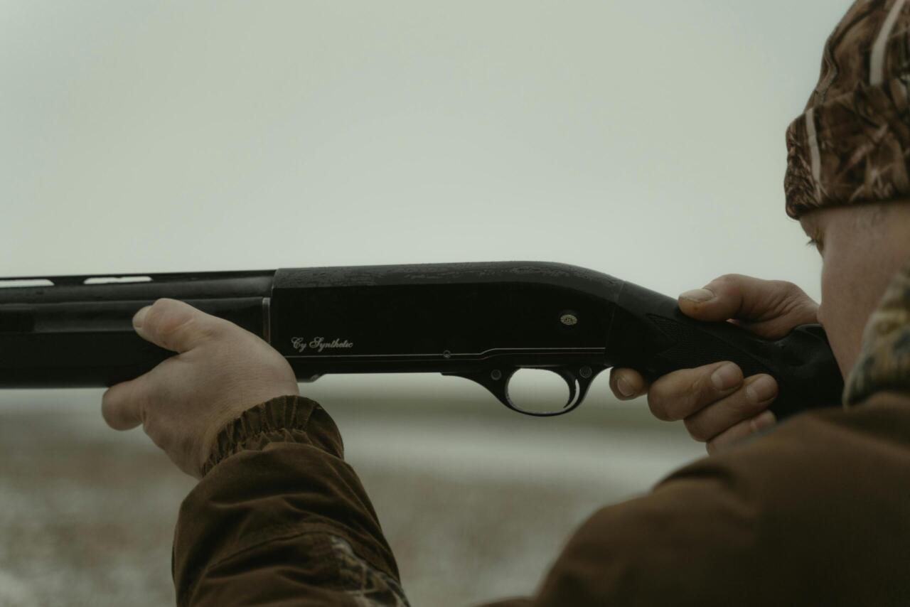 Close-up of a man holding a shotgun ready to aim outdoors, ideal for hunting themes.